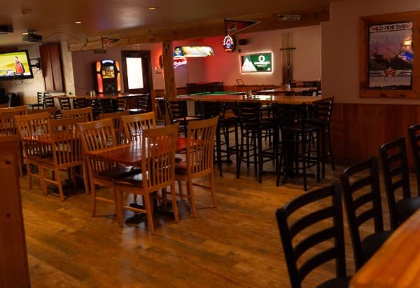 The Golden Tee arcade cabinet lit up beyond the high-top tables and the pool table