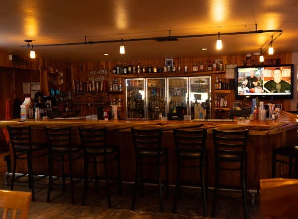 The bar at the Crooked Cowboy — a long wooden bar lined with stools, taps and bottles behind it, and a TV showing the game