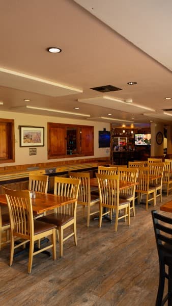 Freshly set tables inside the Crooked Cowboy — light wood chairs, new flooring and framed western prints along the wall