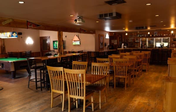 The dining room at the Crooked Cowboy — tables and high-tops set across the floor, the pool table on one side and the bar at the far end